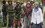 2009年、新疆ウイグル自治区で撮影。中国武装警察を背景に立つウイグル族の女性2人（PETER PARKS/AFP/Getty Images）