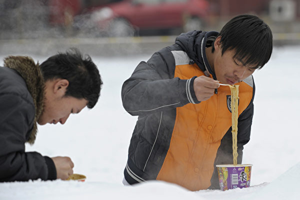 クレディ・スイスの中国人エコノミストは、中国国内の即席麺販売の回復は消費者の節約志向を反映したと指摘。写真は雪が降る日、観光客2人が北京市天安門広場でインスタント麺を食べている様子（LIU JIN/AFP/Getty Images）
