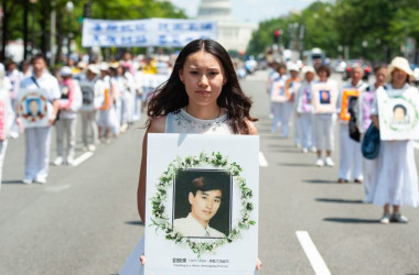 2014年7月17日、法輪功学習者がワシントンDCに集結し、迫害停止を呼びかける集会とパレードを行った。中国共産党の迫害によって死亡した法輪功学習者の写真を手に持つ女性（Larry Dye /The Epoch Times）