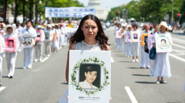 2014年7月17日、法輪功学習者がワシントンDCに集結し、迫害停止を呼びかける集会とパレードを行った。中国共産党の迫害によって死亡した法輪功学習者の写真を手に持つ女性（Larry Dye /The Epoch Times）