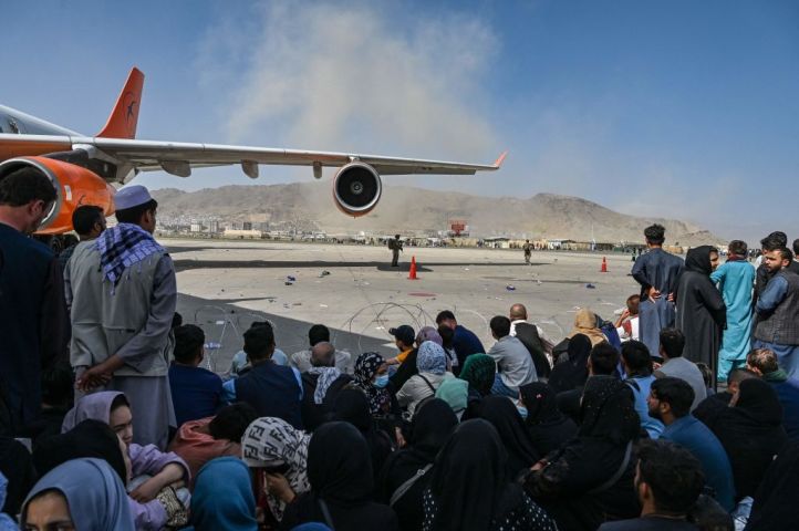 2021年8月16日、カブールの空港で出国を待つアフガニスタンの人々が座っている。20年に及んだアフガニスタンの戦争が驚くべき速さで終結し、タリバンの支配から逃れようと、何千人もの人々が空港に押し寄せた。(Photo by WAKIL KOHSAR/AFP via Getty Images)