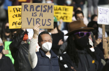 2021年3月13日、ワシントン州シアトルで行われた、アジア人に対するヘイトクライムに反対する集会で、「人種差別はウイルスだ(Racism is a Virus)」と書かれたサインを掲げる男性 (Jason Redmond/AFP via Getty Images)