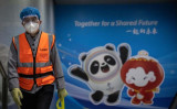 北京の清河駅前で、2022年北京冬季オリンピックの宣伝ボードの前を歩く清掃員 （Carl Court/Getty Images）