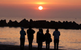 県仙台市の海岸で11日、犠牲者への祈りを捧げながら日の出を見つめる人々（Photo by STR/JIJI PRESS/AFP via Getty Images）